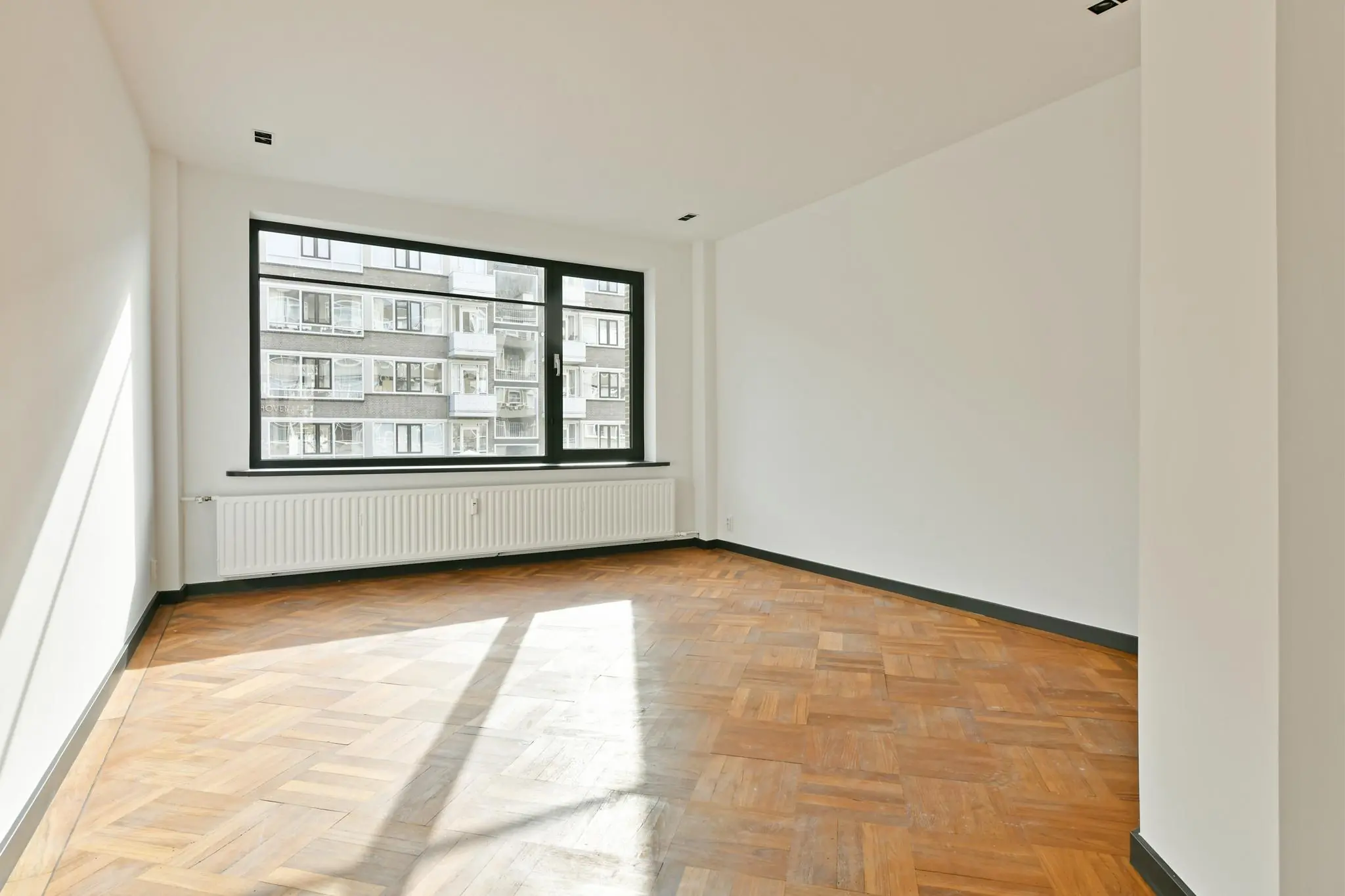 Lichte, lege kamer met visgraat houten vloer en groot raam aan de Cornelis Dopperkade.